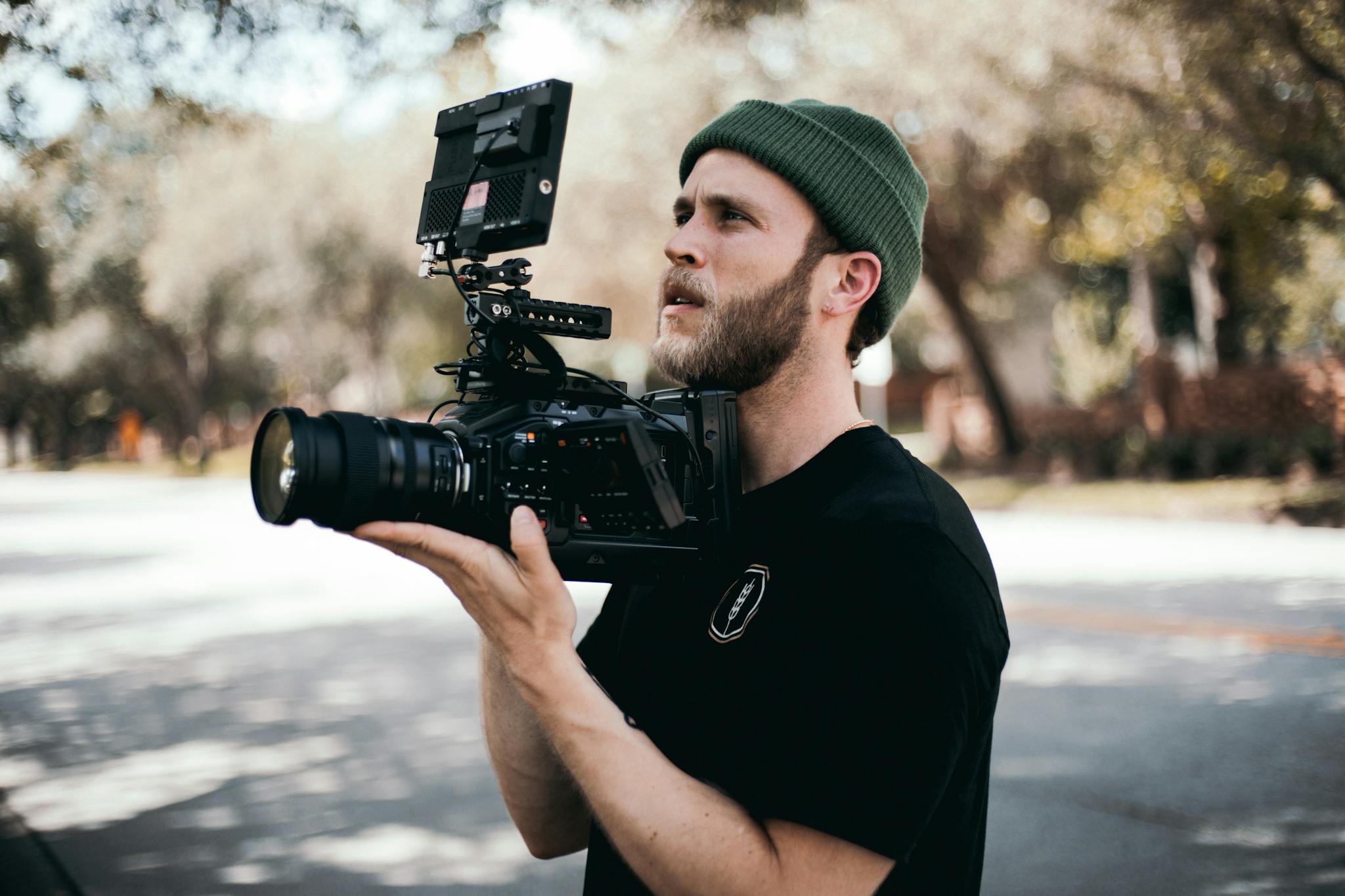 A focused bearded man in a beanie filming outdoors using advanced camera gear.