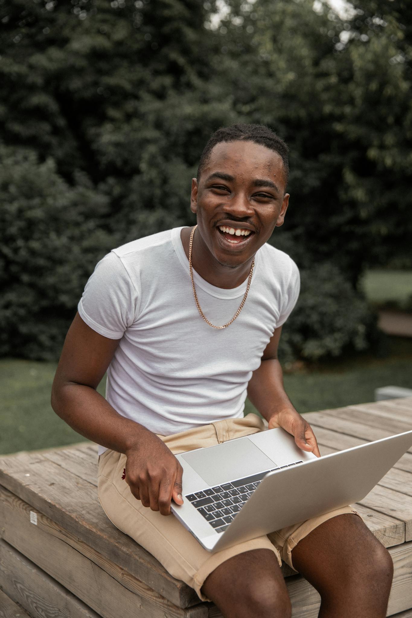 A joyful young man using a laptop outdoors on a sunny day.