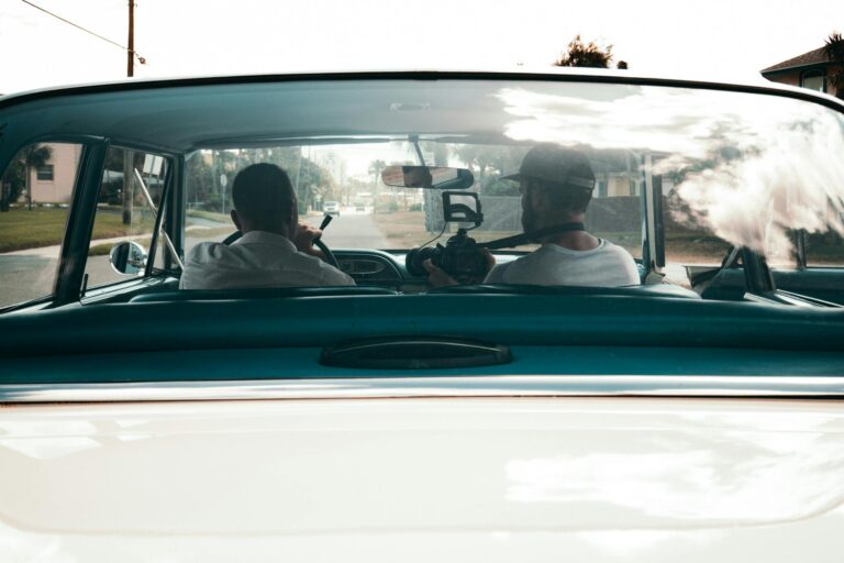 Two filmmakers capturing scenes from a vintage car interior.